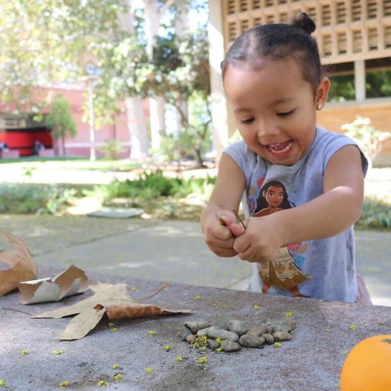 Small child at UC Riverside campus playing with leaves and rocks