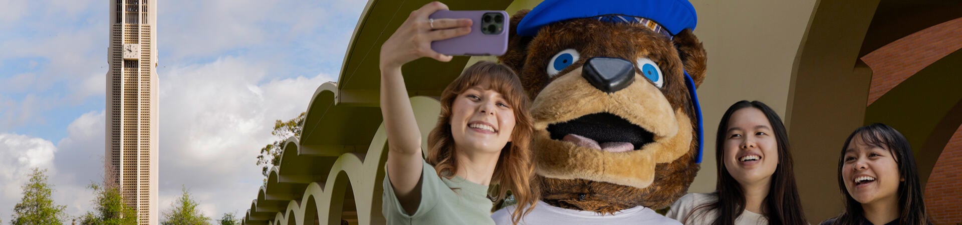 UCR students taking a selfie with Scotty with the Bell tower and Rivera Arches behind them.