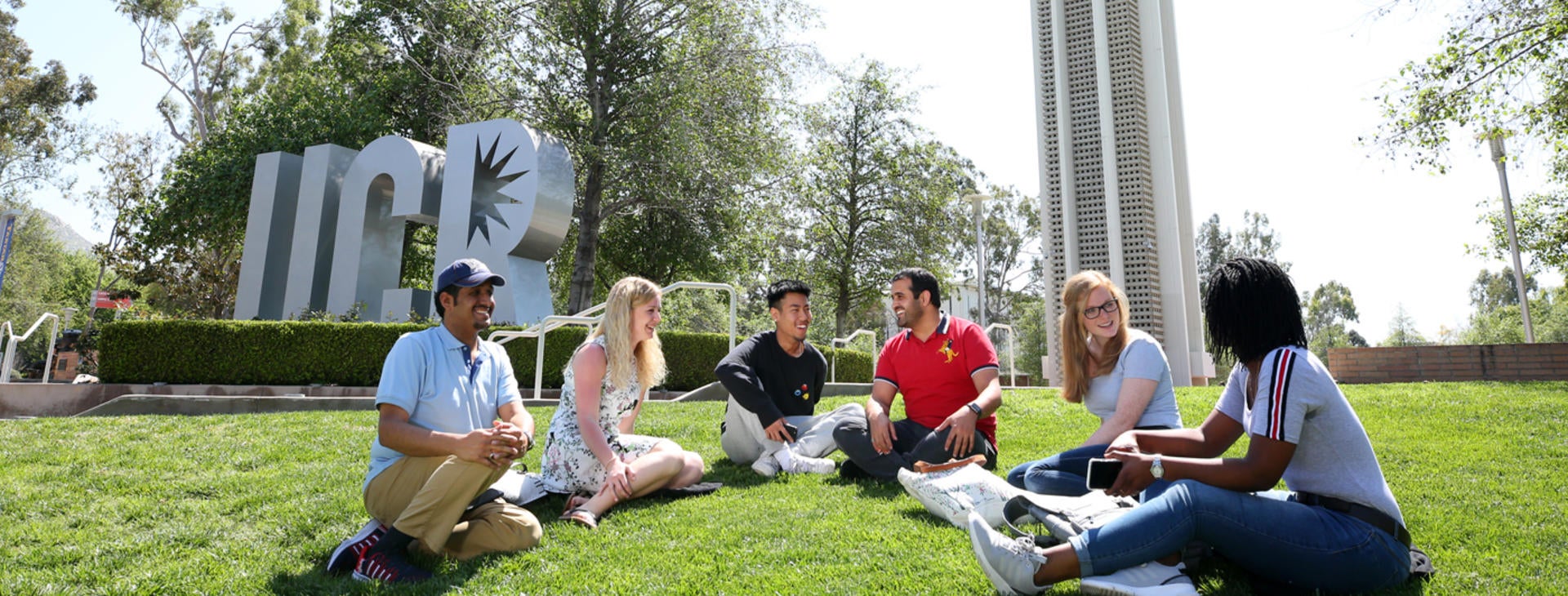 Students sitting on the gras in front of the bell tower